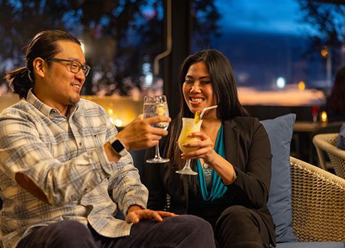 A man and woman toasting drinks on a patio.