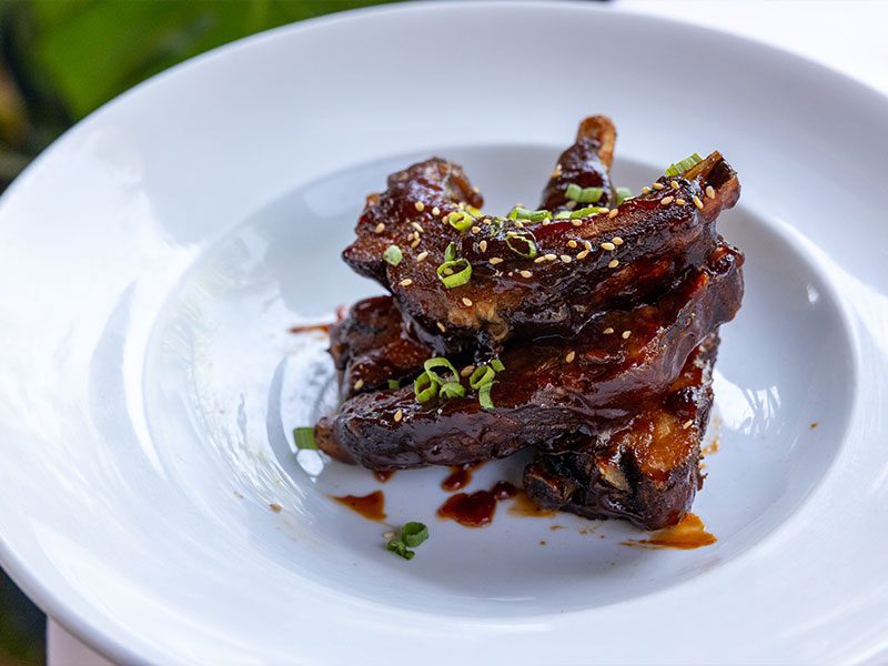 A plate of glazed, grilled ribs garnished with chopped green onions and sesame seeds.