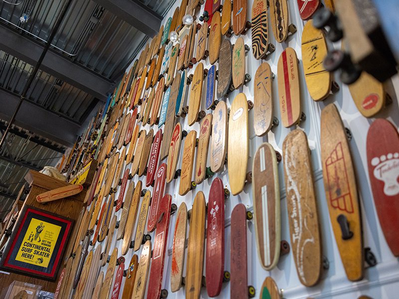 A wall display of various vintage skateboards arranged closely together, with a sign indicating a Continental Surf Skater space.